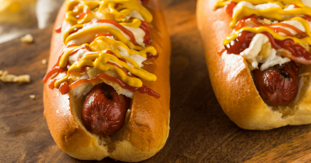 Two hot dogs with ketchup and mustard on a wooden cutting board.
