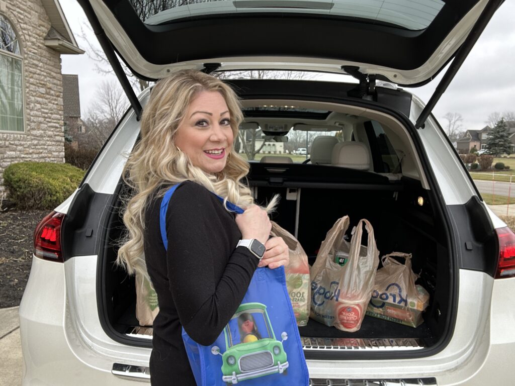 Katie Cooksey with Kroger Krazy standing next to an open trunk full of kroger groceries